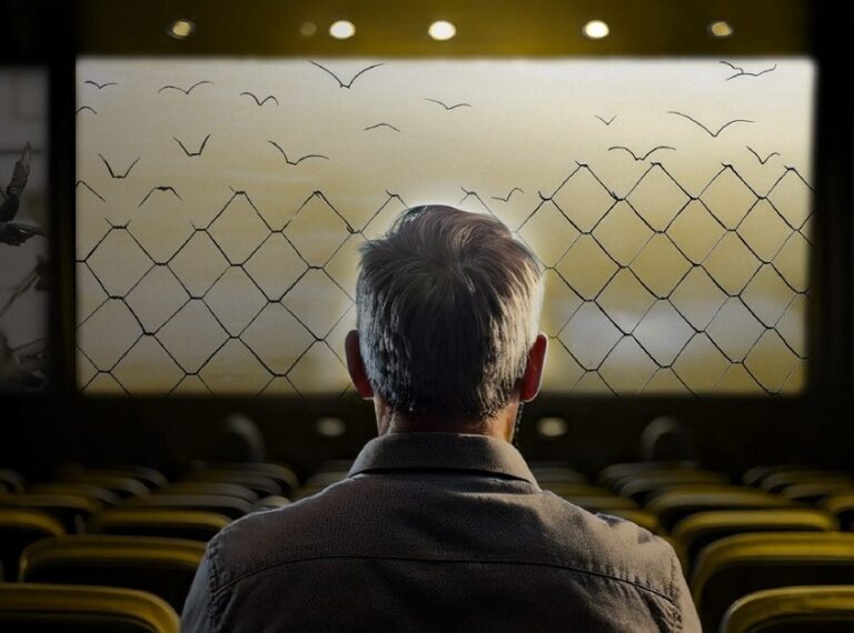 En la foto, un hombre mira del otro lado de una alambrada como vuelan las aves