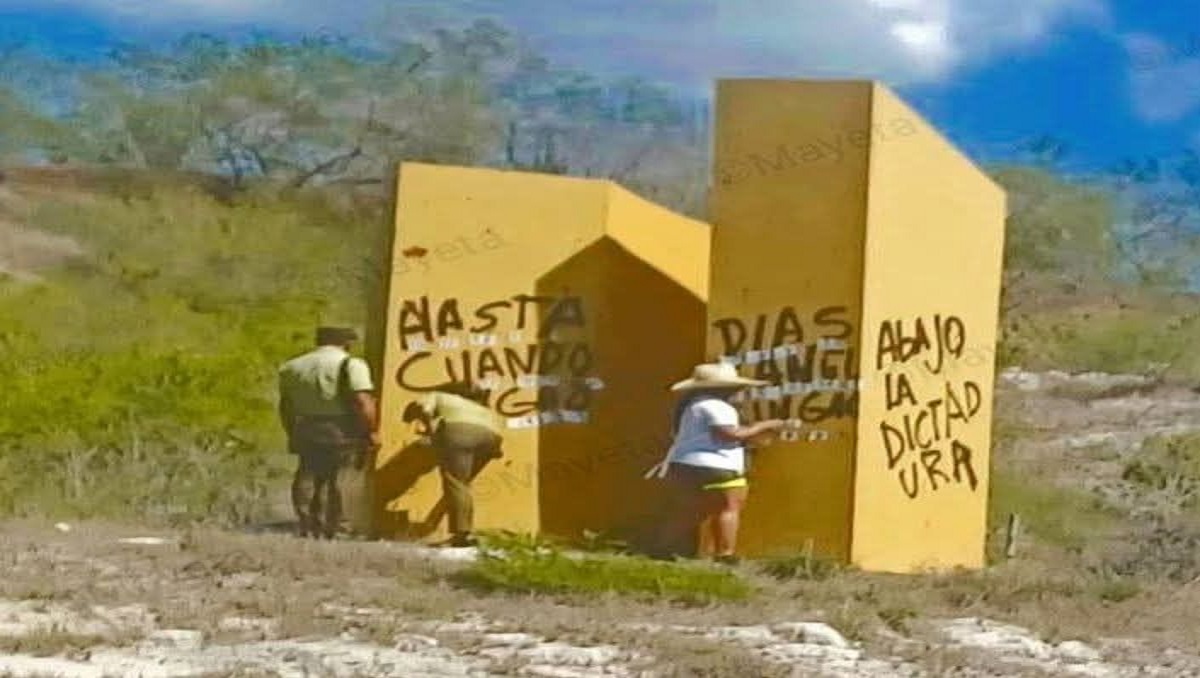 En la foto se ven unos letreros contra la dictadura en unos muros amarillos