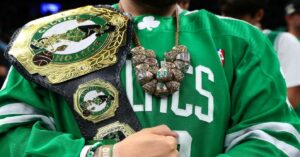 En la foto se ve una persona acariciando un cinturón de Boston Celtics con muchos anillos colgando del cuello