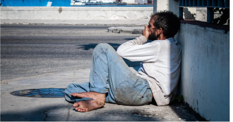 En la foto se ve un hombre, con porte de mendigo, en una acera