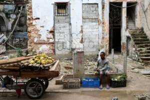 En la foto, un vendedor de alimentos en Cuba frente a una edificación en ruinas, en La Habana