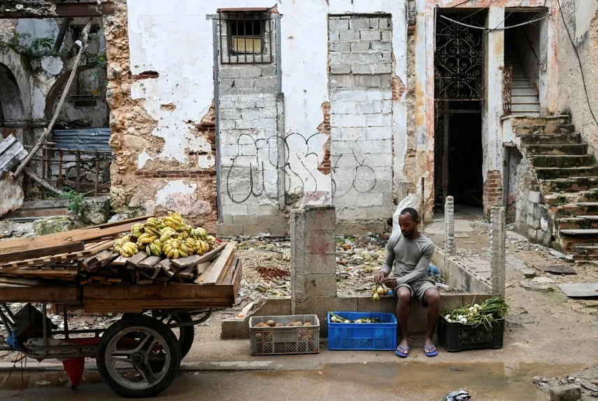 En la foto, un vendedor de alimentos en Cuba frente a una edificación en ruinas, en La Habana