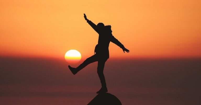 En la foto, una persona intenta equilibrarse sobre un promontorio, con el sol de fondo