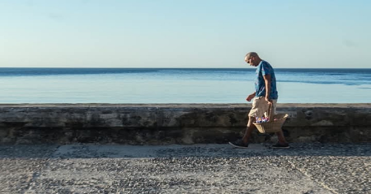 En la foto, un vendedor ambulqante camina cabzbjo por el Malecón
