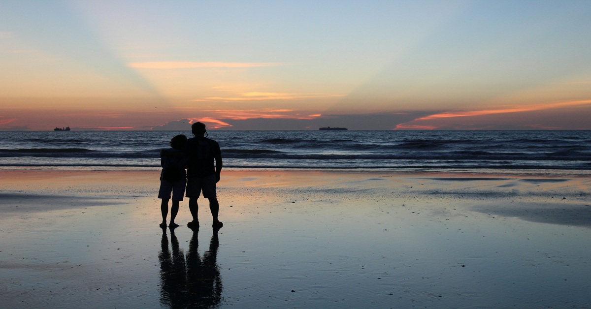 En la foto, una pareja frente al mar al anochecer
