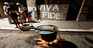 En la foto, unos cubanos cocinan en la calle, con un cartel detrás que dice que viva Fidel