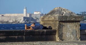 En la foto, una mujer duerme sobre el malecón con El Morro de La Habana de fondo