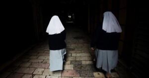 En la foto, dos monjas caminan por un pasillo oscuro