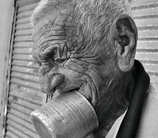 En la foto, un anciano sostiene un jarro en su boca