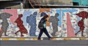 En la foto, un hombre pasa frente a una pared con hombres de colores en La Habana