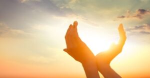 En la foto, unas manos intentan atrapar un sol que nace, que sube