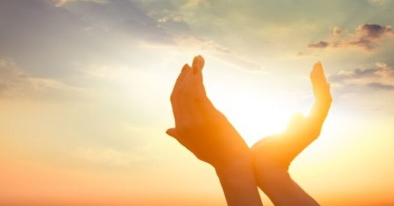 En la foto, unas manos intentan atrapar un sol que nace, que sube