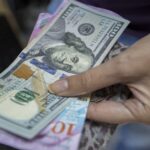 En la foto, una persona sostiene dólares en la mano