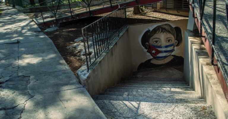 En la foto, un dibujo en una pared de una niña con la boca tapada con una bandera cubana
