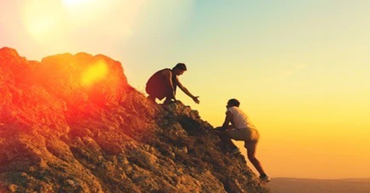 En la foto, una persona ayuda a otra a subir algún promontorio