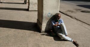 En la foto, un anciano recostado a una columna en una acera