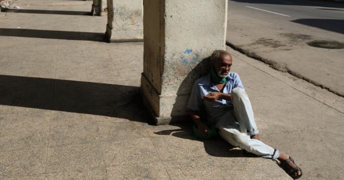 En la foto, un anciano recostado a una columna en una acera