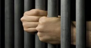 En la foto, las manos de un hombre agarradas a una reja