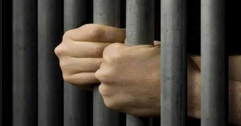 En la foto, las manos de un hombre agarradas a una reja