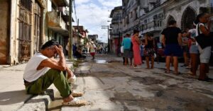 En la foto, personas esperan por algo en una calle de Cuba