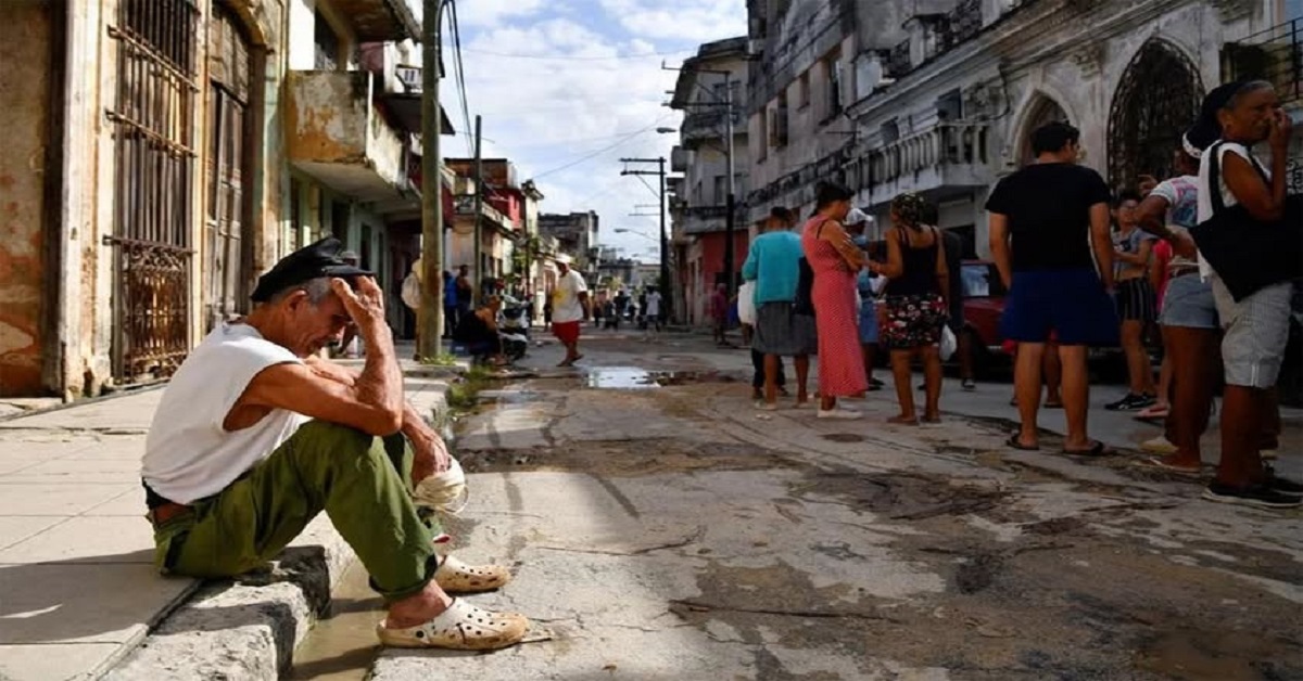 En la foto, personas esperan por algo en una calle de Cuba
