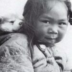 En la foto, una niña inuit carga en la espalda un cachorro