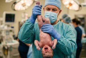 En la foto, un médico sostiene por los pies a un niño al momento de nacer