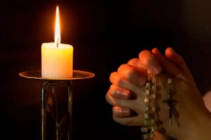 En la foto, una mujer ora en la oscuridad, a la luz de una vela