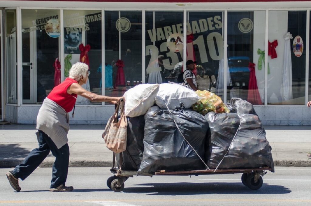 En la foto, una anciana carga latas vacías en una carretilla en La Habana
