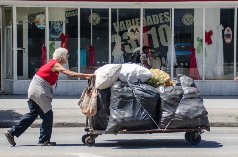 En la foto, una anciana carga latas vacías en una carretilla en La Habana