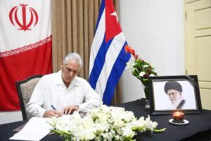 Miguel Díaz-Canel firma el libro de condolencias por la muerte de Ali Jamenei en la embajada de Irán en La Habana, junto a un retrato del líder iraní con una vela y flores blancas.
