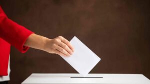 En la foto, una mano de una mujer deposita un voto en una urna