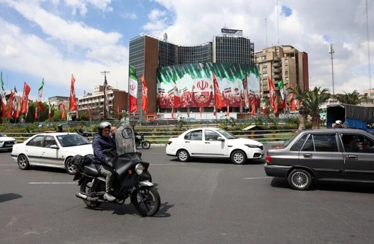 En la foto, Ciudadanos iraníes pasan en coche junto a una gran valla publicitaria política con banderas nacionales de Irán en la plaza Valiasr de Teherán