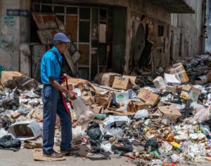 En la foto, un hombre camina delante de un enorme basurero en La Habana