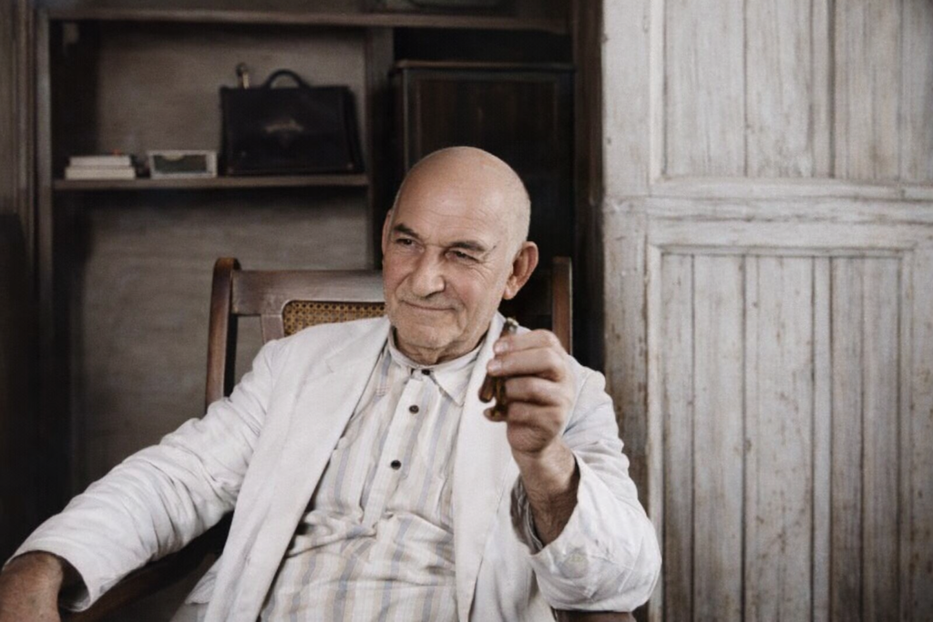 Ángel Castro Argiz sentado en una silla de madera, sosteniendo un cigarro en su mano, en un ambiente interior rústico