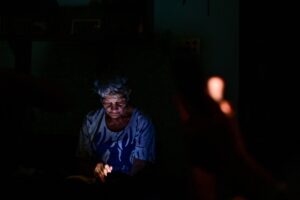 En la foto, una madre cubana mira un teléfono a oscuras en Cuba