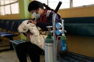 En la foto, una mujer sostiene a un niño al lado de un botellón de Oxígeno