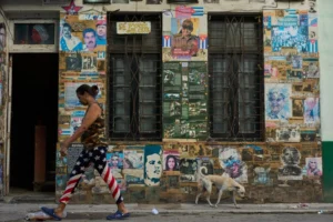 En la foto, una mujer con un pantalón con la bandera de EEUU camina ante fotos con símbolos del castrismo