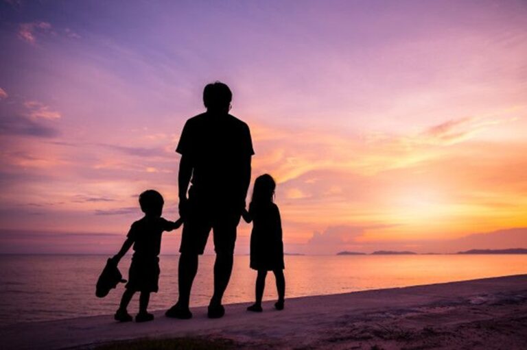 En la foto, un padre con sus hijos, en silueta