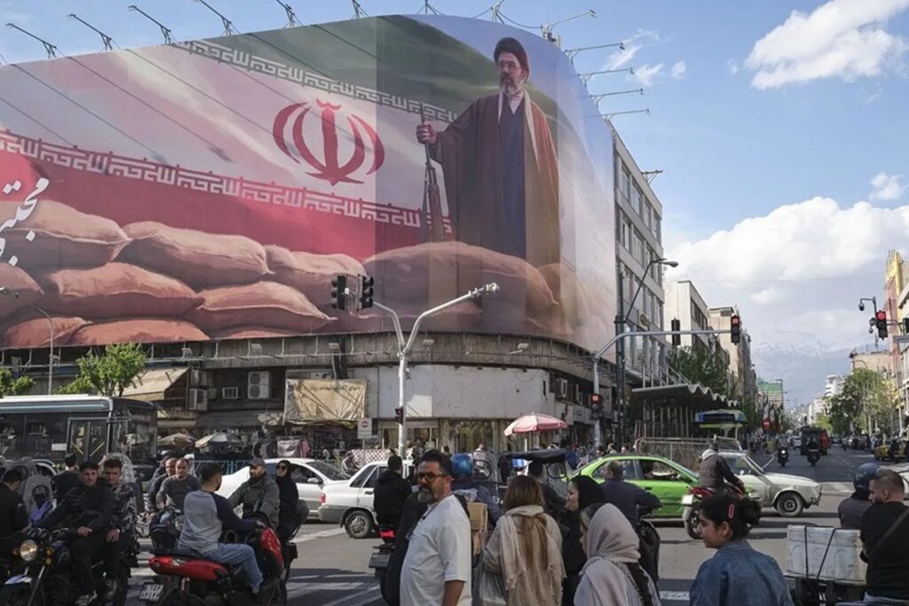 En la foto, Un grupo de personas camina delante de un cártel del líder supremo de Irán Mojtaba Jameneí en el centro de Teherán