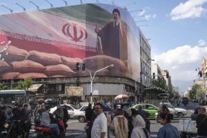 En la foto, Un grupo de personas camina delante de un cártel del líder supremo de Irán Mojtaba Jameneí en el centro de Teherán