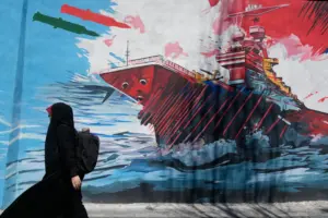 En la foto, una mujer pasa ante un mural que muestra un portaviones estadounidense atacado, en Teherán