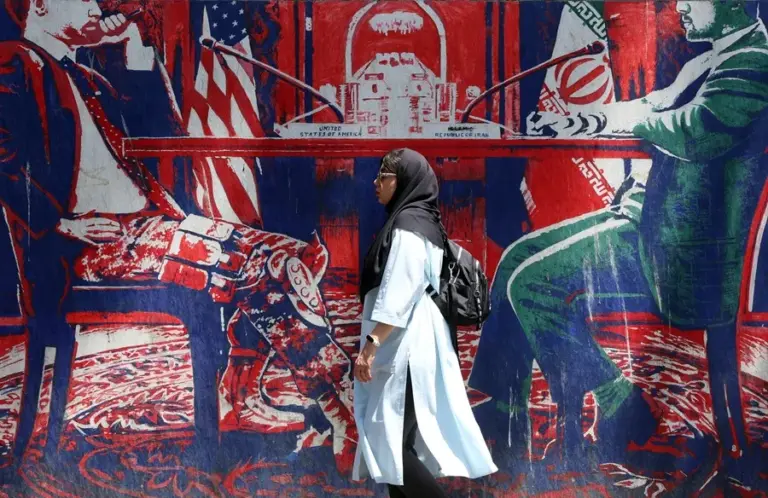 En la foto, una mujer caminando frente a un mural antiestadounidense sobre las negociaciones, cerca de la ex embajada de Estados Unidos, en Teherán (Irán