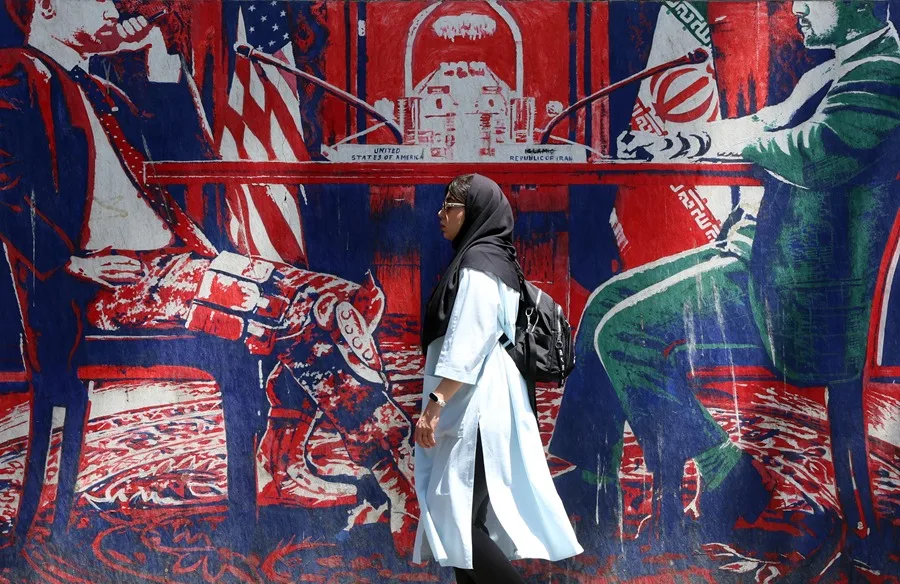 En la foto, una mujer caminando frente a un mural antiestadounidense sobre las negociaciones, cerca de la ex embajada de Estados Unidos, en Teherán (Irán