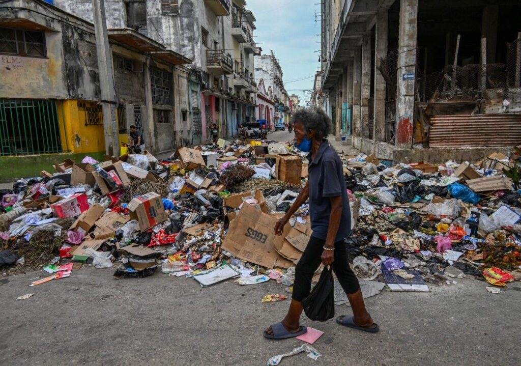 En la foto, un hombre pasa ante un enorme basurero en La Habana