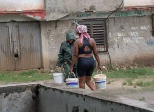 En la foto, mujerres acarrean agua de lluvia bajo un aguacero