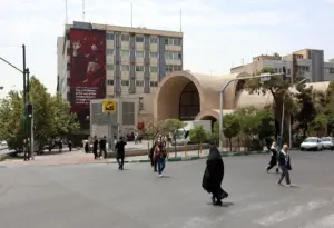 En la foto, iraníes caminando junto a una valla publicitaria contra EE.UU. e Israel, en una calle de Teherán