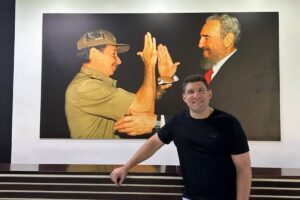 En la foto, Raúl Guillerm Rodríguez Castro posa ante una foto de su abuelo y Fidel Castro