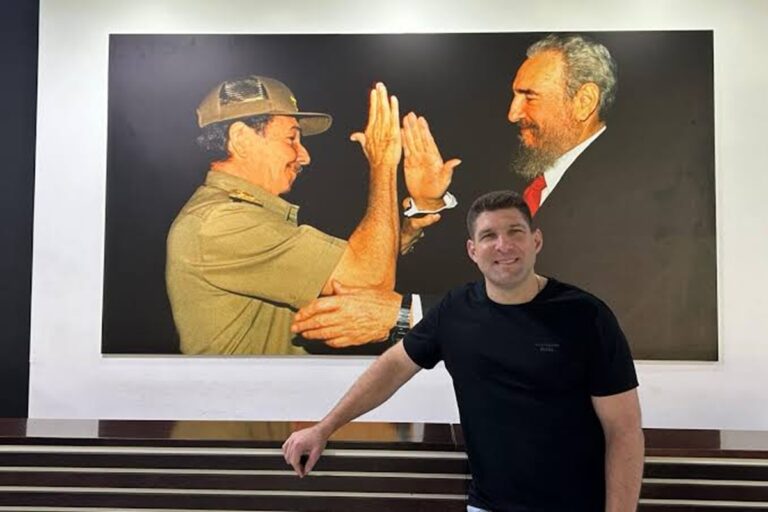 En la foto, Raúl Guillerm Rodríguez Castro posa ante una foto de su abuelo y Fidel Castro