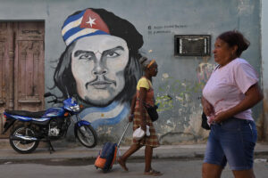 En la foto, dos personas pasan frente a un cartel con una foto del Che Guevara en La Habana